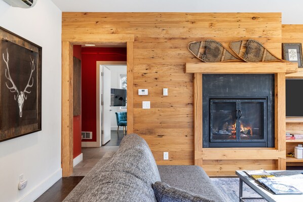 A cozy living room with a fireplace, a sofa, and a framed deer head artwork. - Outpost: King Ridge 7 Penthouse - AC & Hot Tub! (Jackson)