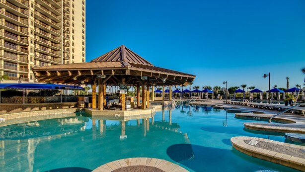 A hotel pool area with a gazebo, multiple swimming pools, and a tall building in the background. - Luxury North Beach Resort home w/ pool/elevator & marsh/ocean view (North Myrtle Beach)