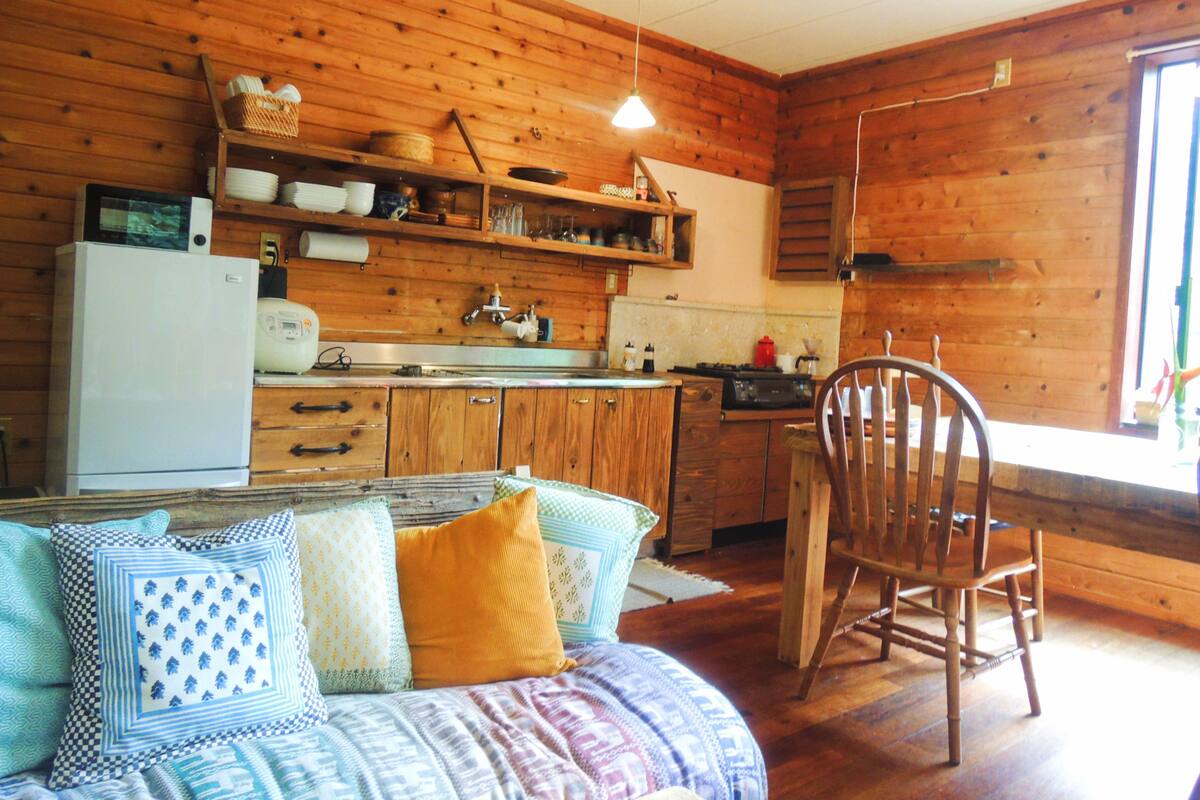 A cozy cabin-style kitchen with wooden walls, a white refrigerator, and a wooden dining table with a chair.
