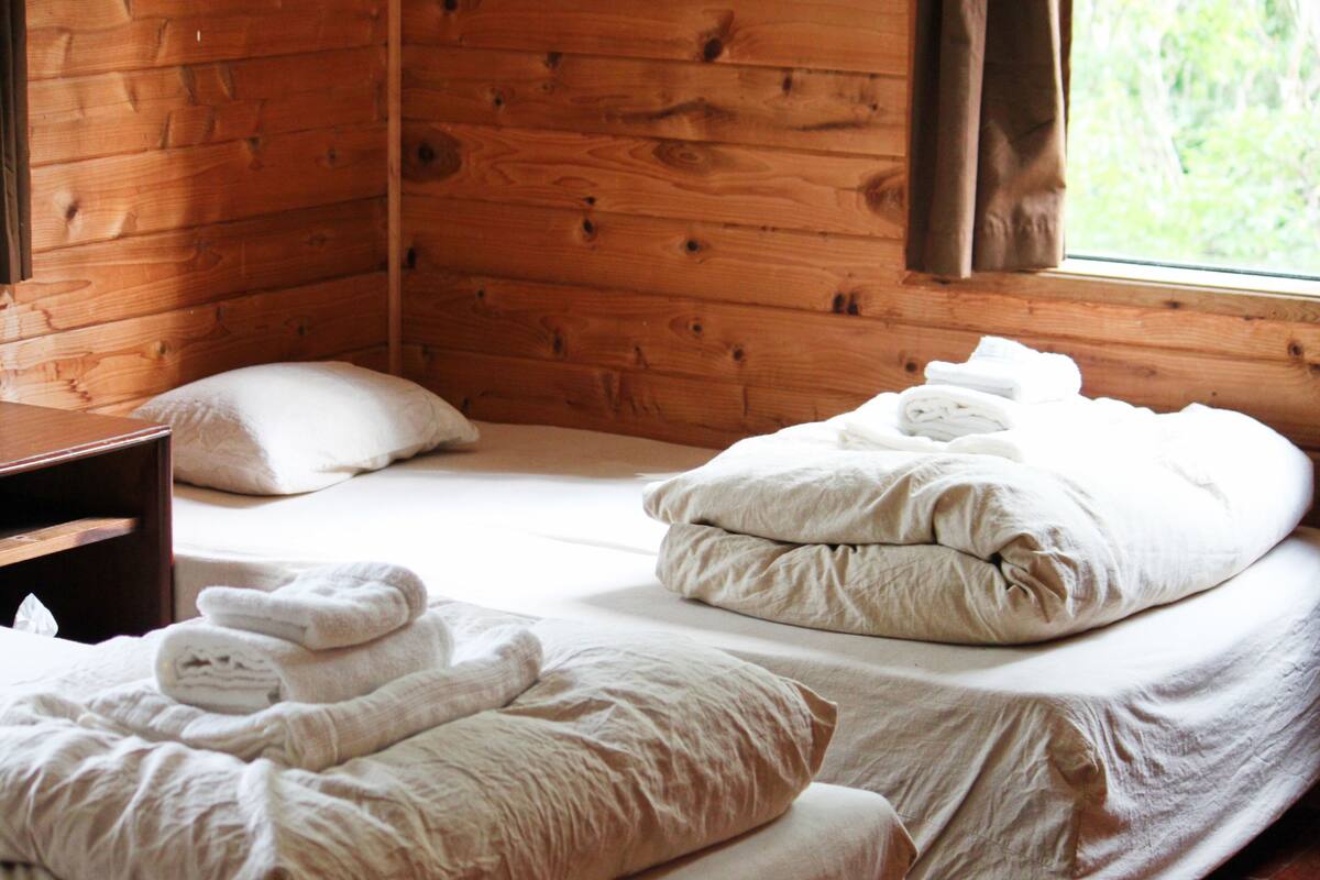 A wooden cabin room with two beds, each with neatly folded towels and pillows.