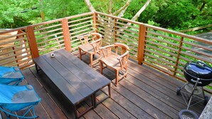 A wooden deck with a table and chairs, surrounded by lush greenery. - Private Lodge COTENCHI (Nakijin)