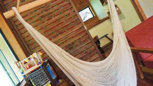 A hammock suspended from a wooden ceiling, a wooden table, and a patterned wall. - Private Lodge COTENCHI (Nakijin)
