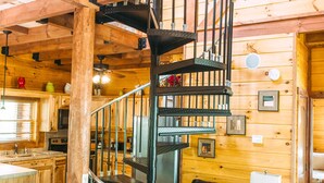 A wooden cabin interior with a spiral staircase, a dining area, and a living room with leather furniture.