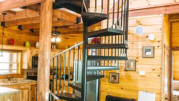 A wooden cabin interior with a spiral staircase, a dining area, and a living room with leather furniture.