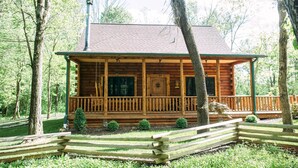 A wooden cabin with a porch, surrounded by trees.