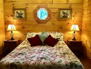 Una camera da letto in legno con copriletto floreale, due lampade e quadri appesi alle pareti.