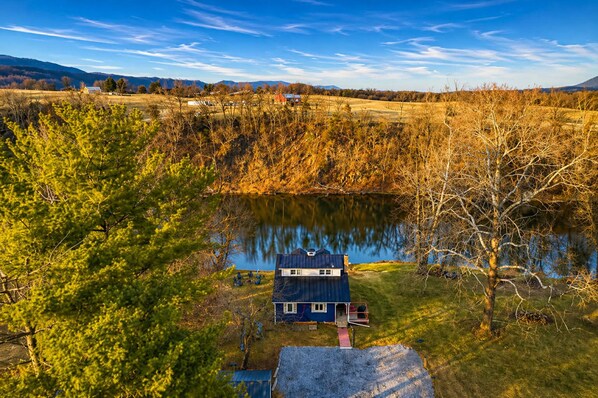 Une cabane dotée d’un petit porche, entourée d’arbres et bordée par un lac.