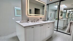 Une salle de bain moderne avec un grand miroir, deux vasques et une cabine de douche en verre.