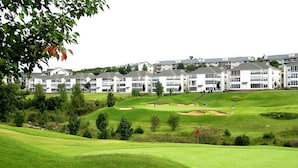 A golf course with a clubhouse and residential buildings in the background.