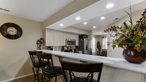 A modern kitchen with a white countertop, bar stools, and stainless steel appliances.