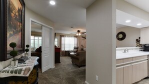A spacious living room with a large painting, a dining area with a table set for four, and a kitchen with modern appliances.
