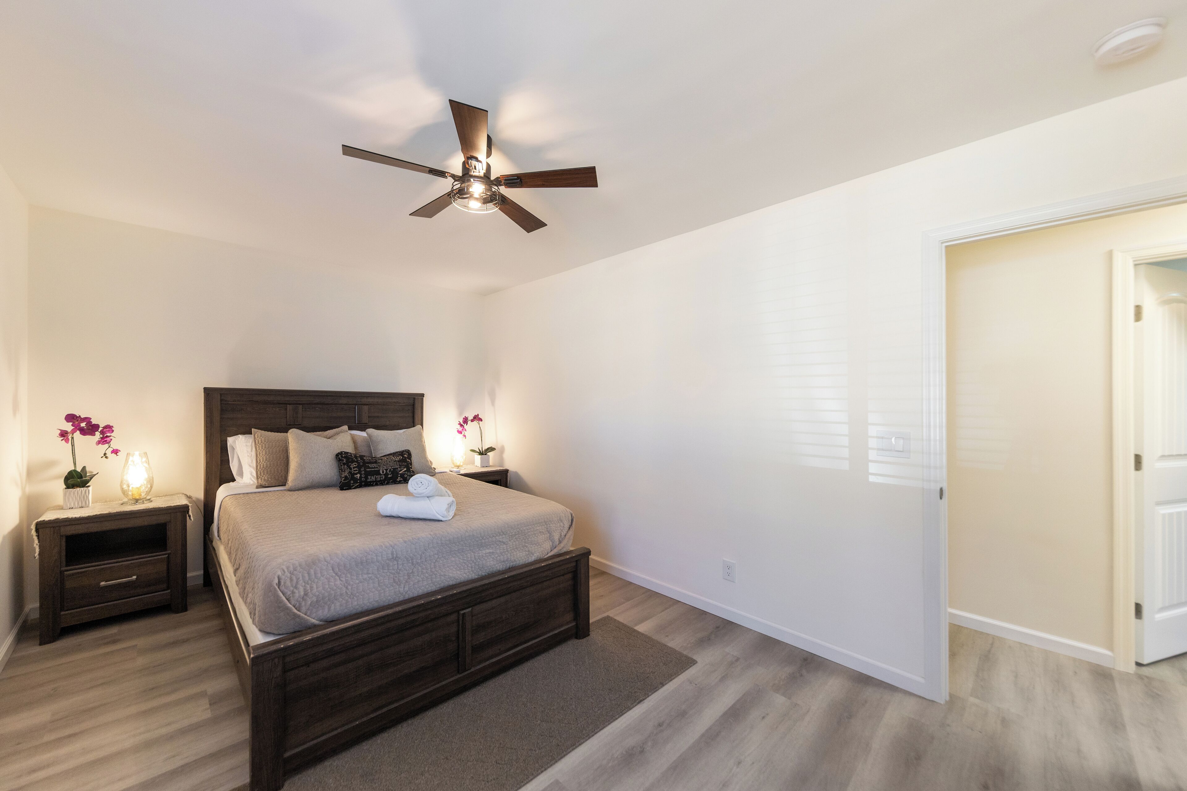 A bedroom with a bed, nightstands, a ceiling fan, and a door.
