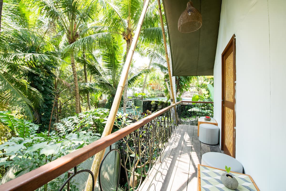 Una terraza de madera con barandilla metálica que da a un jardín exuberante con diversas plantas y árboles.