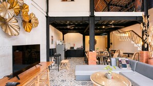 A spacious living area with a sofa, a round table with plants, a television, and a kitchen in the background. - Ubud Tropical - Hostel (Ubud)