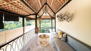 A balcony with a patterned floor, a round table, and a cushioned seating area. - Ubud Tropical - Hostel (Ubud)