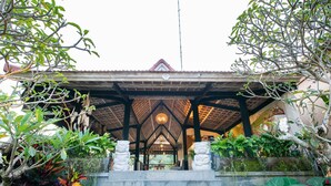 A traditional building with a thatched roof, stone steps leading up to a covered entrance, and lush greenery surrounding the structure. - Ubud Tropical - Hostel (Ubud)