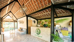 A reception area with a tropical theme, including a reception desk, seating area, and a large window offering a view of the outdoors. - Ubud Tropical - Hostel (Ubud)