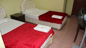 A hotel room with two beds, each with a red bedspread and white linens. There is a nightstand between the beds and a standing fan in the corner. - Liwagu Lodge (Ranau)