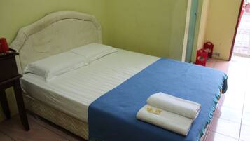 A bed with a white headboard and a blue bedspread, a red cup on a small table, and a door with a red stool outside.