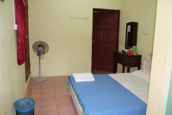 Quarto com uma cama, um ventilador, uma porta de madeira, uma mesinha com um espelho e uma cortina vermelha.