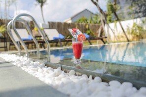 A poolside setting with a glass of red drink, white pebbles, and a metal pool ladder.