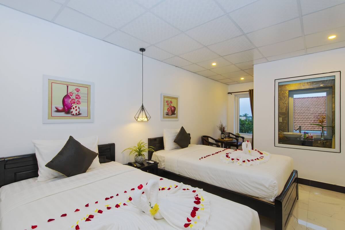 Une chambre d’hôtel avec deux lits, un bureau, une chaise, une plante en pot et des œuvres d’art accrochées aux murs.