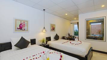 A hotel room with two beds, a desk, a chair, a potted plant, and artwork on the walls.