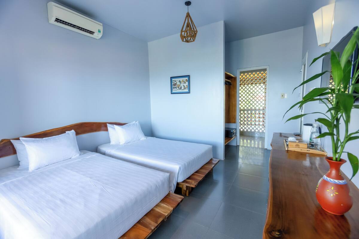 A hotel room with two beds, a wooden nightstand, a potted plant, and a ceiling fan.