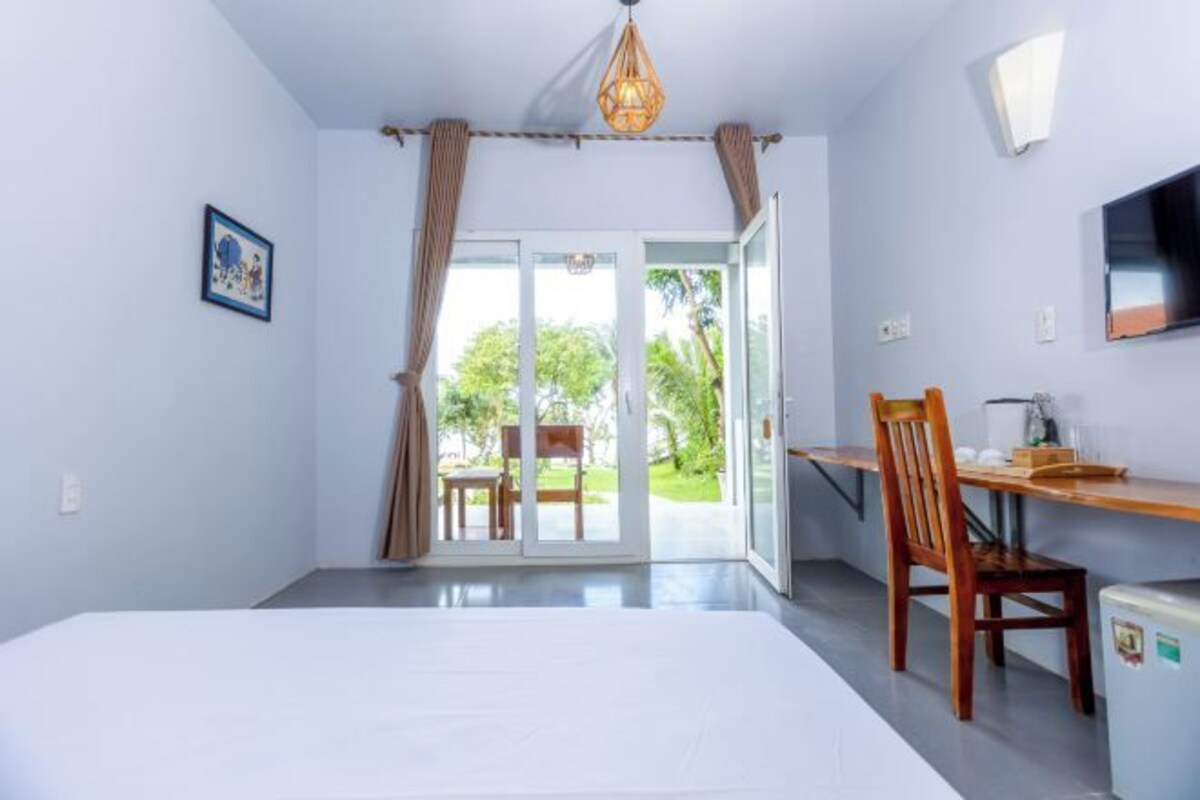 A room with a bed, a desk, a chair, a television, and a sliding glass door leading to an outdoor area.