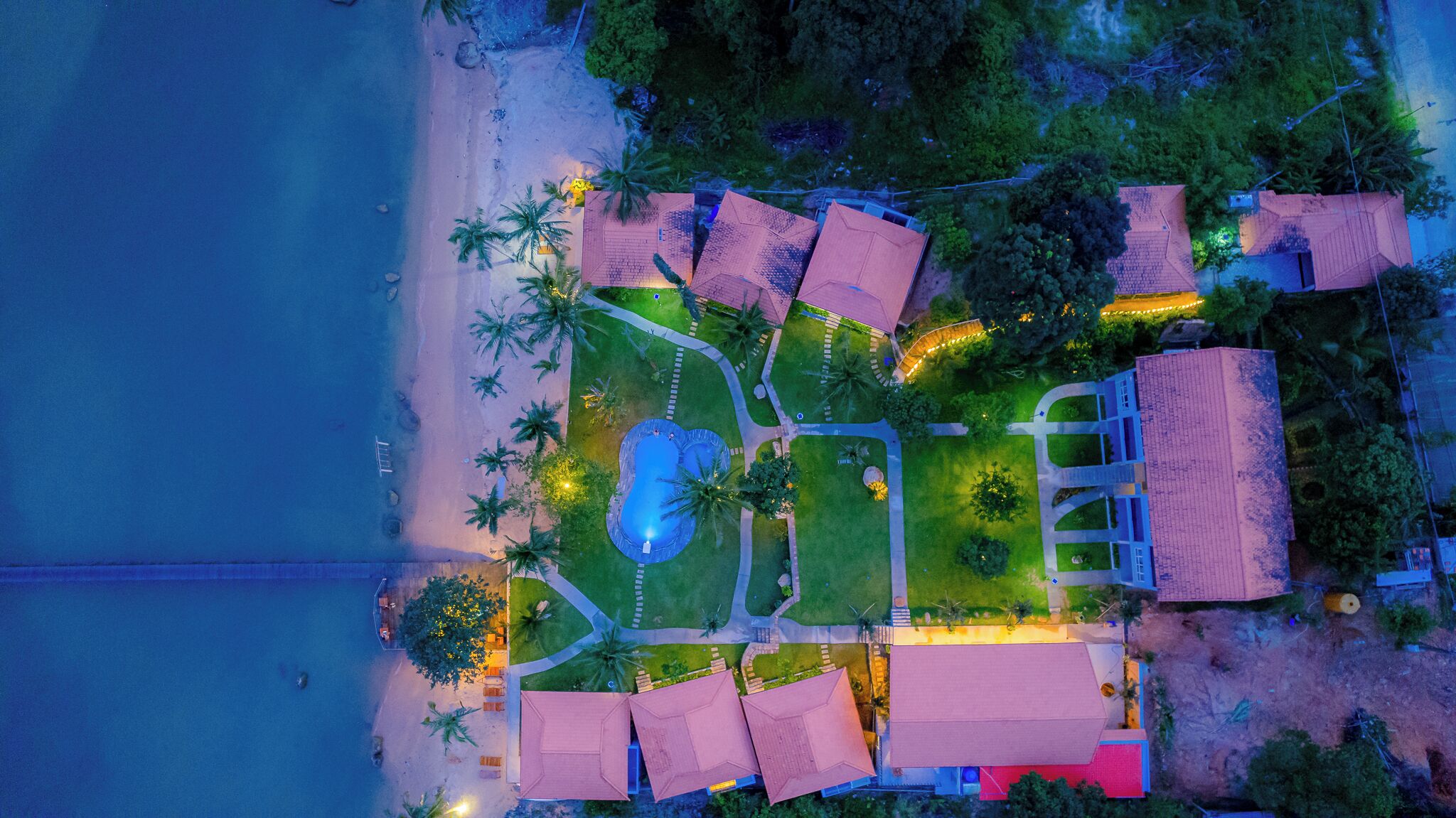 An aerial view of a resort with a pool, beach, and multiple buildings.