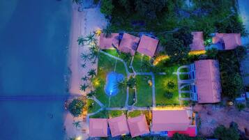 An aerial view of a resort with a pool, beach, and multiple buildings.