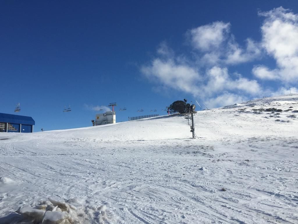 A snowy ski slope with a ski lift and a blue building in the background.