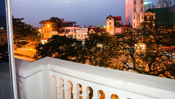 Eine Stadtansicht im Dämmerlicht mit beleuchteten Gebäuden, darunter ein markanter Turm und ein Gebäude mit der Aufschrift 'PROONG NAM AUTO'.