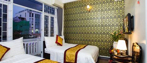 A hotel room with two beds, a sitting area with a chair, a table with a lamp, and a wall-mounted TV.