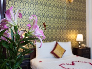 Quarto de hotel com uma cama, uma mesa de cabeceira com abajur e um arranjo de flores.