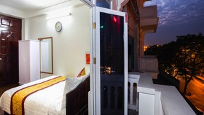 Ein Hotelzimmer mit Bett, Schrank, Wanduhr und einem Balkon mit Blick auf die beleuchtete Stadt.