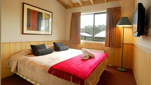A bedroom with a large bed, a television, a window with curtains, and a framed picture on the wall. - Discobulous 6 (Mount Buller)