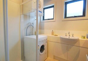 A compact bathroom with a washing machine, a sink, and a window above the mirror. - Discobulous 6 (Mount Buller)