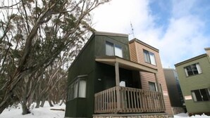 A two-story cabin with a stone foundation, a balcony, and a wooden deck. - Discobulous 6 (Mount Buller)