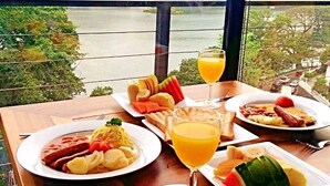 Una mesa con alimentos para el desayuno y un vaso de jugo de naranja, con vista a un lago y edificios al fondo.