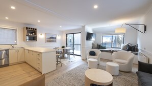 Un appartement moderne comprenant une cuisine, un coin repas et un salon. Il est équipé d’un téléviseur à écran plat, d’une table à manger et d’un canapé.