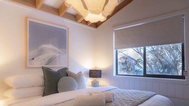 Une chambre avec un grand lit, une fenêtre donnant sur des arbres, un tableau encadré au mur et une lampe de chevet.