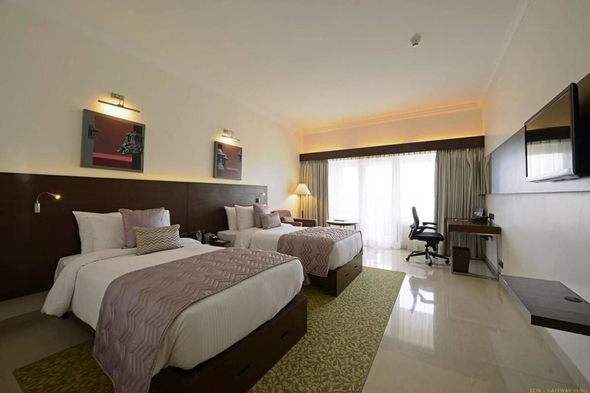 A hotel room with two beds, a desk, a chair, a TV, and artwork on the walls.