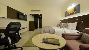 A hotel room with a bed, a desk, a chair, a round table, and a TV mounted on the wall.