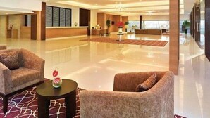 Un hall espacioso con piso pulido, dos sofás, una mesa de recepción y un gran ventanal con vistas a la ciudad.