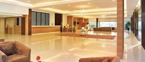 Un hall espacioso con piso pulido, dos sofás, una mesa de recepción y un gran ventanal con vistas a la ciudad.