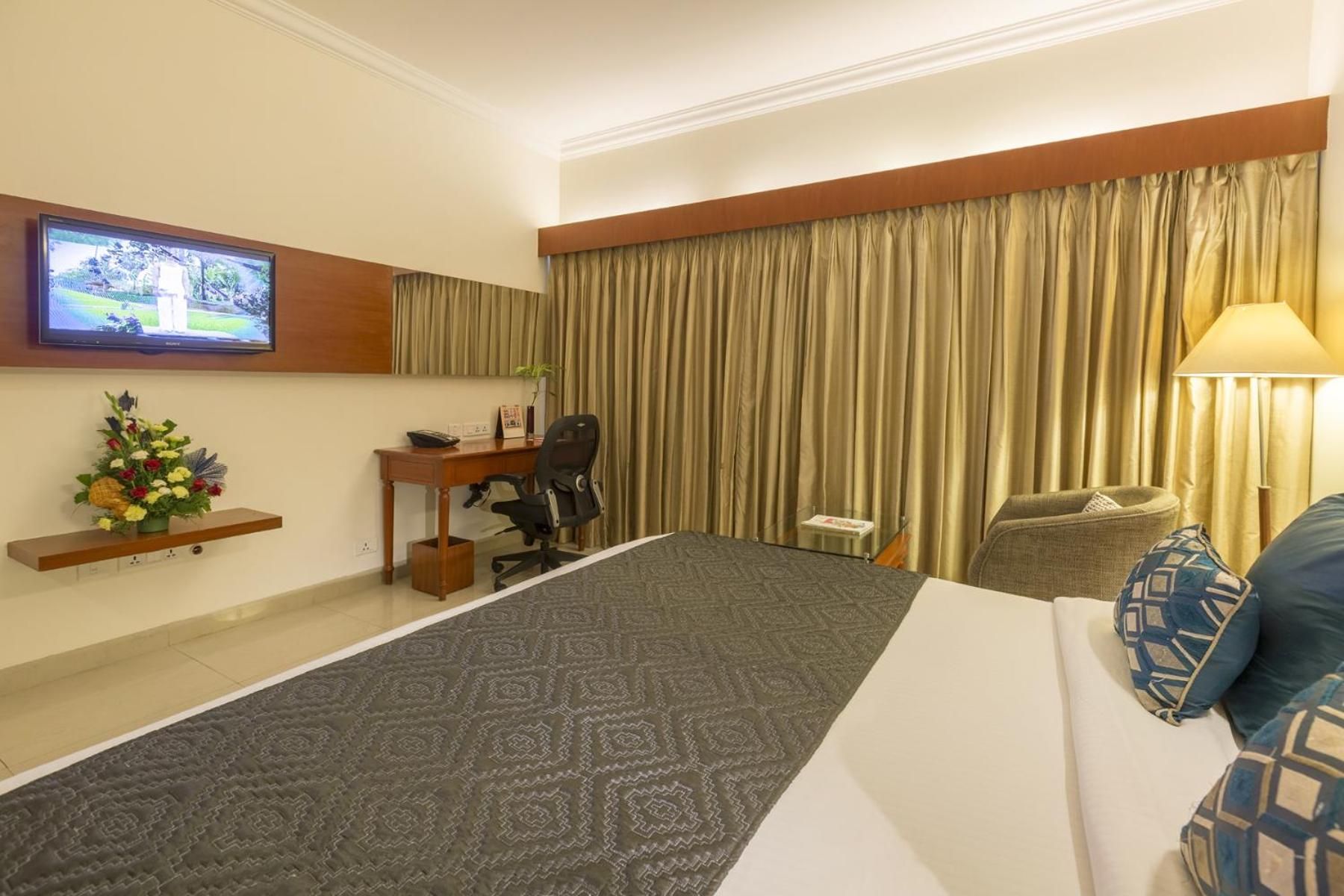 Een hotelkamer met een bed, een bureau, een stoel, een televisie en een raam met gordijnen.