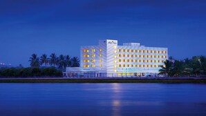 Un hotel moderno con varios pisos y un llamativo letrero que dice 'Hotel', ubicado junto a una masa de agua tranquila con palmeras al fondo.