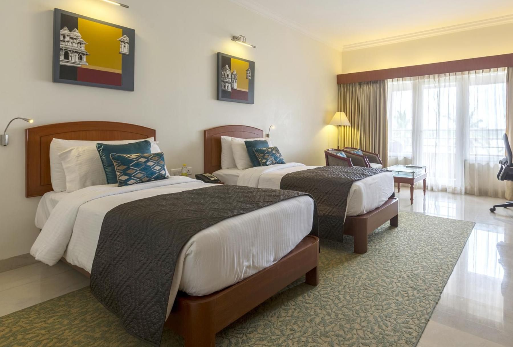 A hotel room with two beds, a desk, a chair, and artwork on the walls.