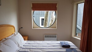 Une chambre à coucher avec un lit, une fenêtre donnant sur l’extérieur, un radiateur et une table de chevet.